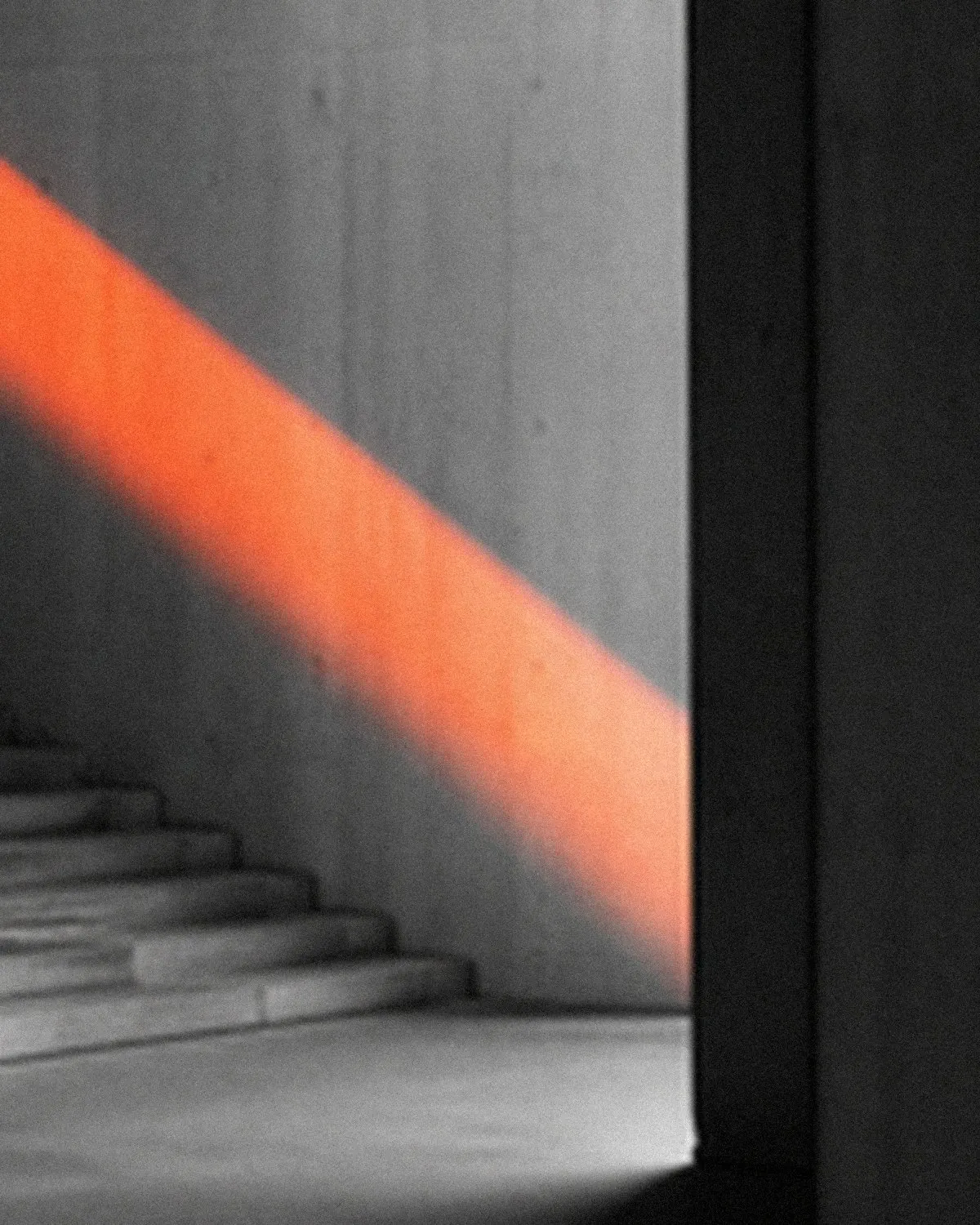 Una lama di luce arancione su un muro di cemento, accanto a una scala